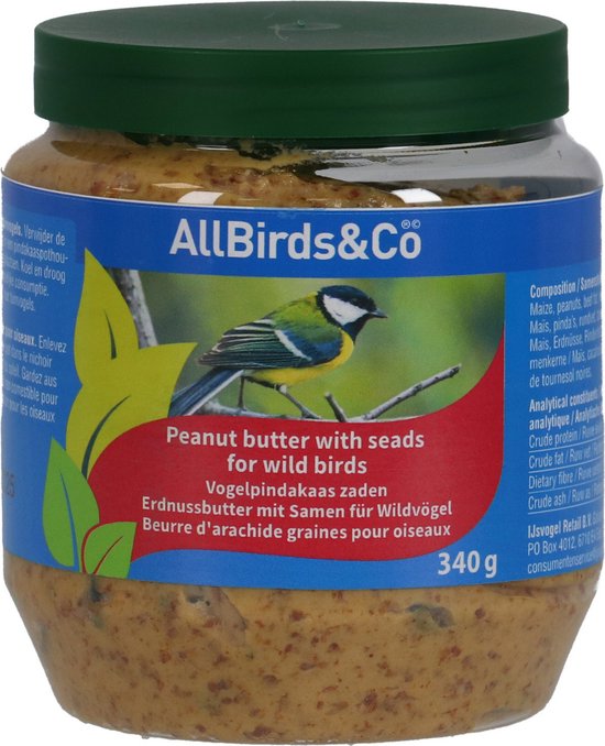 Pot pindakaas met zaden voor vogels, met een koolmees op een tak.