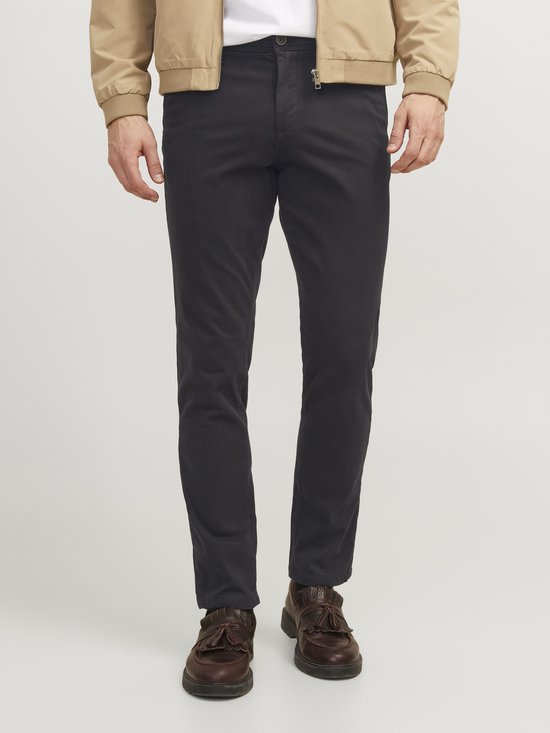 Man in zwarte chino broek met bruine loafers en een beige bomberjack.