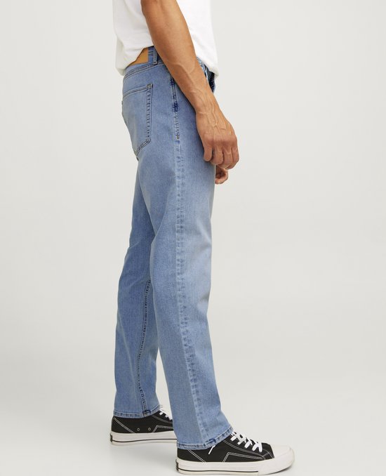 Man in lichtblauwe jeans, staand in profiel.