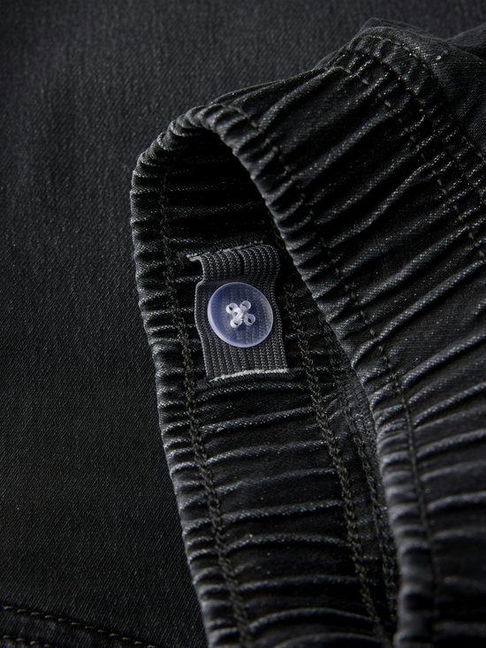 Sluiting van de tailleband van een zwarte jeans met een verstelbare knop.