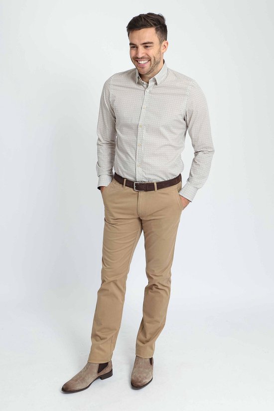 Man met de handen in de zakken, draagt een beige overhemd met een subtiel patroon en een bruine riem.
