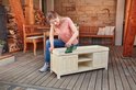 Vrouw schuurt houten kast met groene Bosch multischuurmachine, stofopvangbak bevestigd.