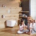 Mère et fille dans une salle de bain avec WC suspendu et porte-brosse WC. Murs en bois.