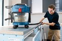 Vakman gebruikt een blauwe Bosch GAS 18V-10 L stofzuiger met slang om een werkblad schoon te zuigen.