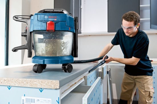 Vakman gebruikt een blauwe Bosch GAS 18V-10 L stofzuiger met slang om een werkblad schoon te zuigen.