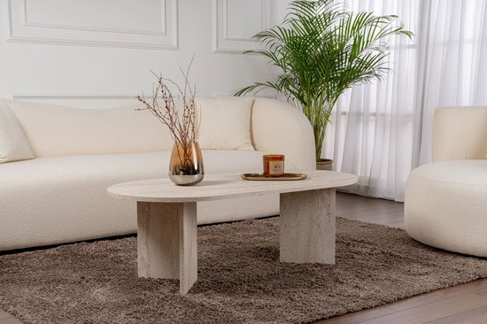 Ovale salontafel met travertijnlook, naast een witte bank en een groene plant.