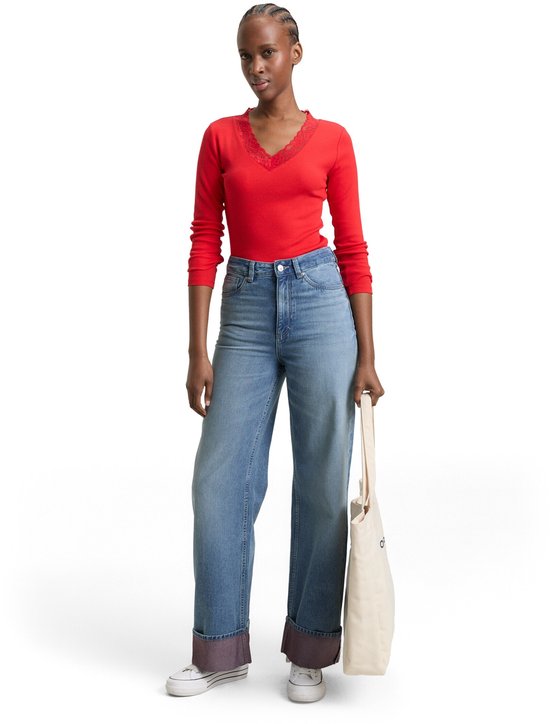 Model in een rode longsleeve met kanten detail en een wijde, lichtblauwe jeans met omgeslagen zoom.