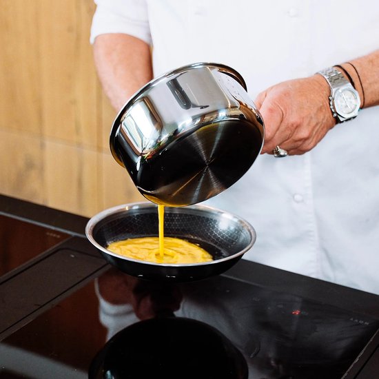 Chef giet gekleurd beslag in een zilverkleurige koekenpan op een inductiekookplaat.