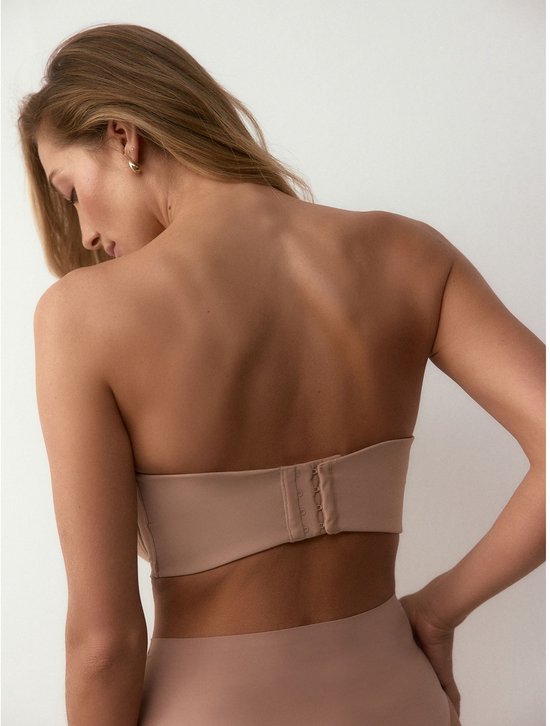Achterkant van een model in beige strapless bh en slip. De sluiting van de bh is zichtbaar.