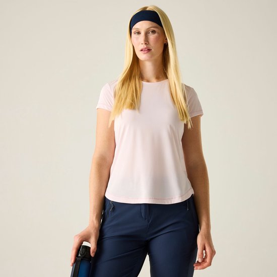 Model met blond haar en donkere haarband, draagt lichtroze sportshirt en marineblauwe sportbroek.