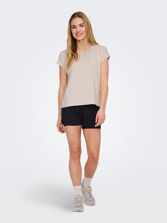 Model staat naar voren in beige sportshirt met korte mouwen en zwarte short.
