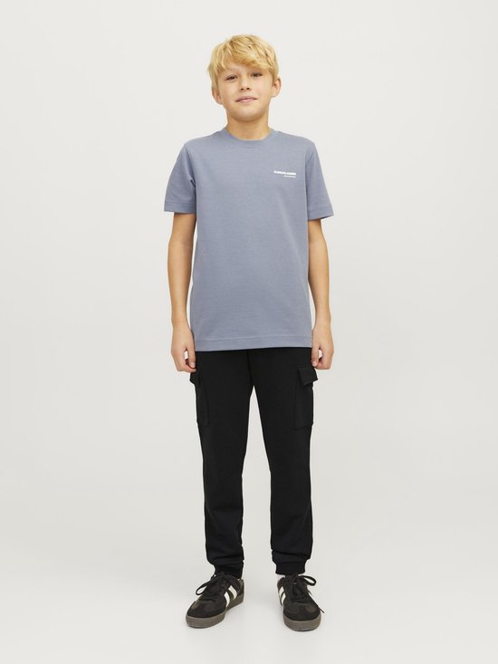 Jongen in grijze t-shirt en zwarte cargobroek, staand.