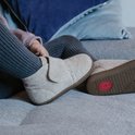 Een meisje op een bank, draagt beige vilten slofjes met klittenband en grijze legging.