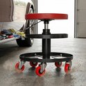 Werkplaatskruk met rode zitting en zwart frame, met twee ronde planken en rode zwenkwielen, naast een auto.