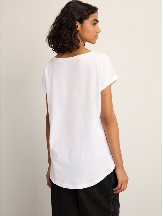 Een vrouw met krullend donker haar draagt een wit T-shirt met opgerolde korte mouwen en een ronde hals, van achteren gezien.