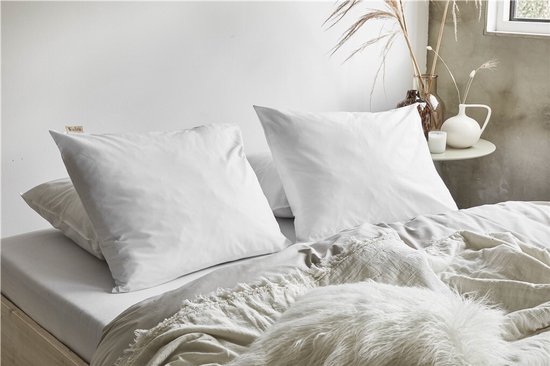 Twee witte kussenslopen op een bed, met een plaid en sierkussen.