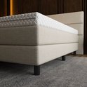 Gedetailleerde weergave van een beige boxspring, met een matras met honingraatpatroon en een gedeelte van het gestreepte hoofdbord.