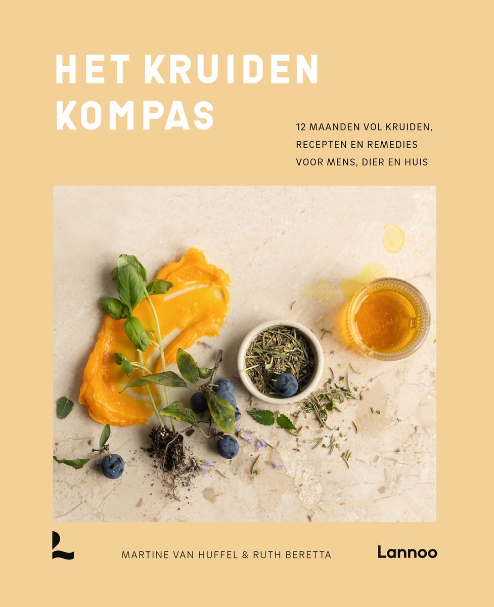Kookboek "Het Kruiden Kompas" met een compositie van oranje puree, kruiden, blauwe bessen en een glas amberkleurige vloeistof op een marmeren ondergrond.