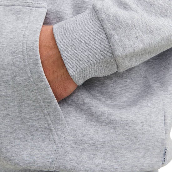 Close-up van een hand in de zak van een lichtgrijze hoodie met rits. 'JACK & JONES' label zichtbaar.