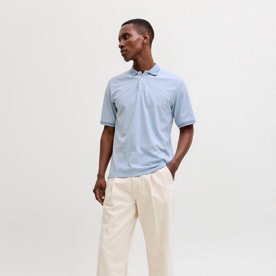 Man in lichtblauw poloshirt met witte kraag en manchetten, beige broek.