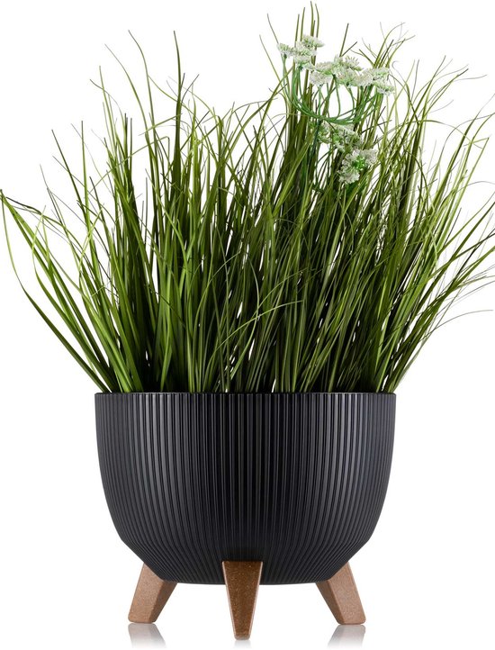 Zwarte plantenpot met ribbels en bruine pootjes, gevuld met lange groene grassprieten en witte bloemetjes.