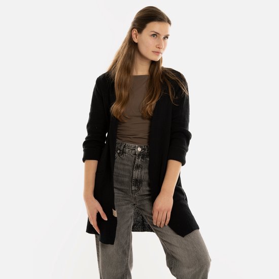 Model draagt een lang, zwart gebreid vest over een bruine top en grijze jeans.