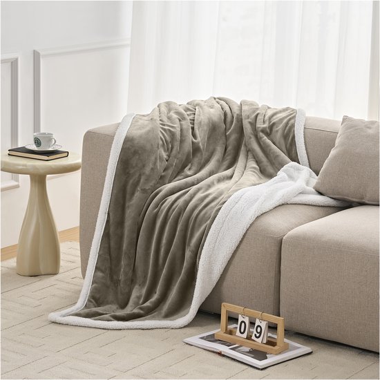 Taupe fleece plaid met witte sherpavoring, gedrapeerd over een bank.
