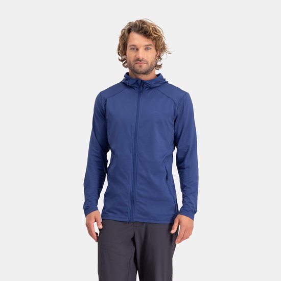 Man met golvend haar draagt een donkerblauwe hoodie en grijze broek, kijkt naar voren.