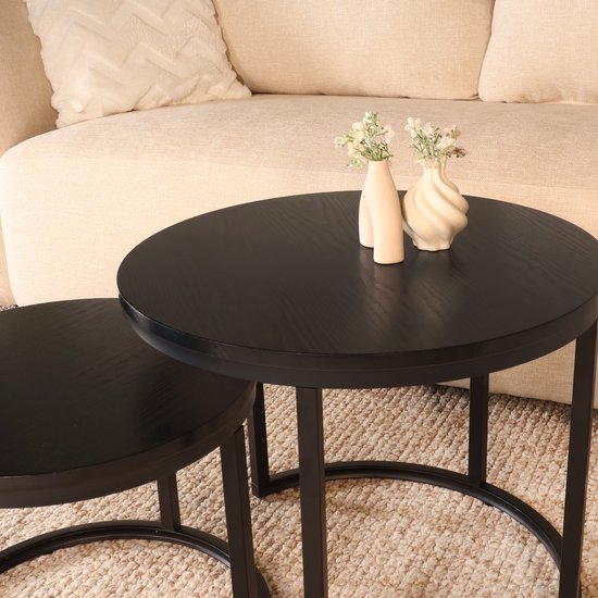 Twee ronde zwarte bijzettafels, de grotere met decoratieve vaasjes met bloemen erop.
