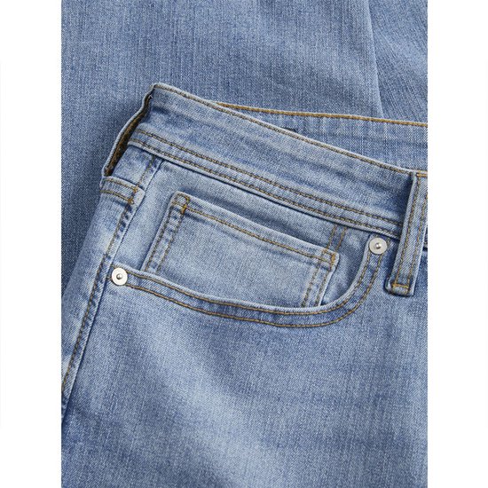 Detailopname van de voorkant van een lichtblauwe spijkerbroek. De broek heeft een ritssluiting en een klein zakje.