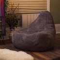 Lila beanbag stoel op een houten vloer, bij een raam met jaloezieën en een vaas met droogbloemen.