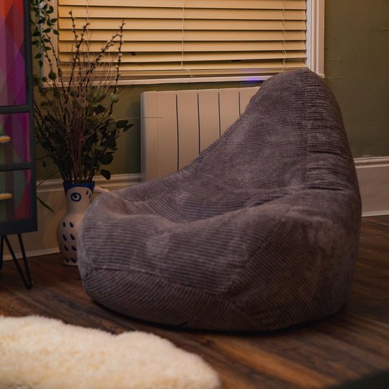 Lila beanbag stoel op een houten vloer, bij een raam met jaloezieën en een vaas met droogbloemen.