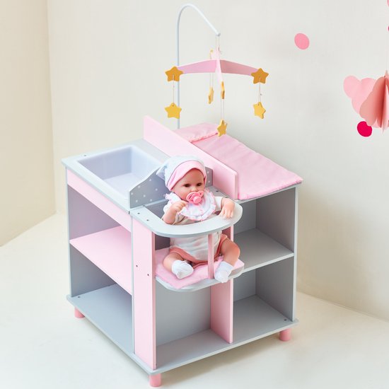 Grijze commode met roze accenten, witte stippen. Een pop met roze slab en muts zit in de kinderstoel. Ernaast liggen gele schoentjes.