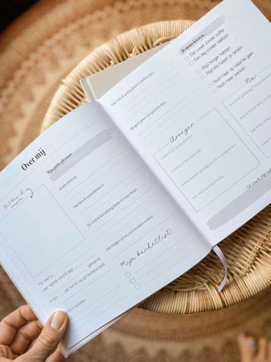 Openstaand vriendenboek op een rieten stoel, een hand houdt een pagina vast met secties 'Over mij' en 'Mijn bucketlist'.