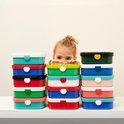 Une fille regarde par-dessus des piles de boîtes à tartines Mepal colorées.