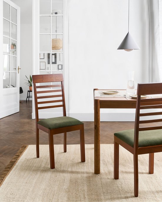 Twee donkerbruine eetkamerstoelen met groene zittingen in een eetkamer op een houten vloer.