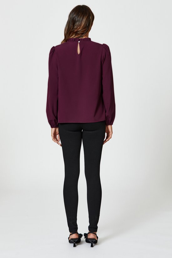 Achterkant van een vrouw in pruimkleurige blouse met hoge hals, ballonmouwen en zwarte skinny jeans.