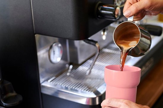 Tasse rose remplie de café provenant d'une machine à expresso.