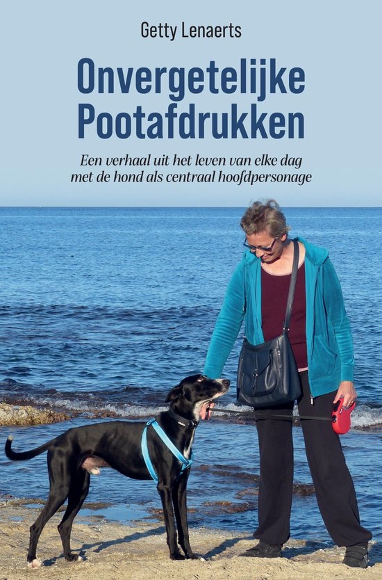 Een vrouw met een blauwe hoodie en een zwarte hond met blauw tuigje bij de zee. Titel: Onvergetelijke Pootafdrukken.