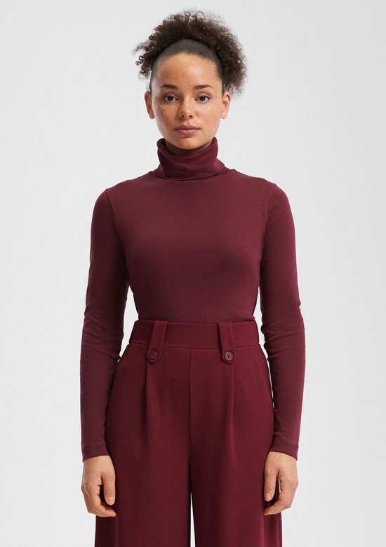 Model draagt een bordeauxrode coltrui en een bordeauxrode broek met hoge taille en knopen.