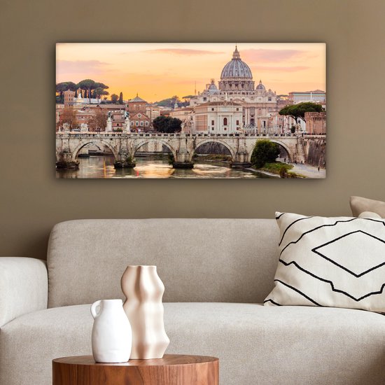 Canvas van de Sint-Pietersbasiliek en de Ponte Sant'Angelo in Rome bij zonsondergang, hangend boven een beige bank.
