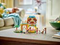 Animalerie LEGO Friends avec un toit en forme de tête de chien, sur une table en bois. Trois mini-poupées, un lapin blanc et un chaton se tiennent devant.