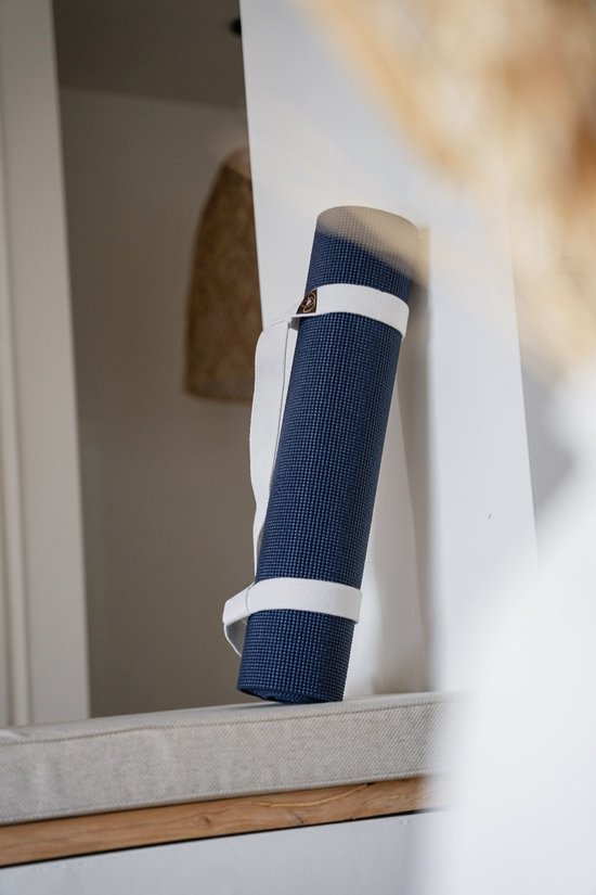 Donkerblauwe, opgerolde yogamat met witte draagbanden, rustend op een gestoffeerd oppervlak.