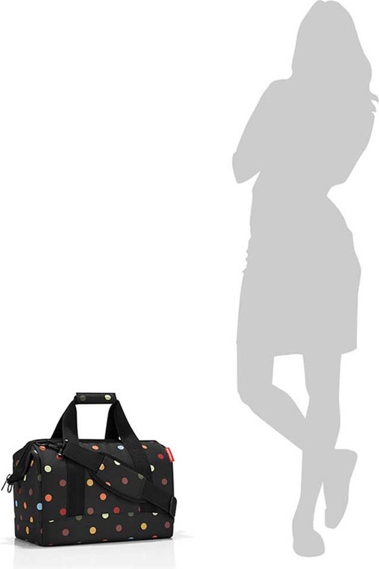 Zwarte reistas met veelkleurige stippen naast een silhouet van een vrouw.
