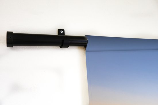Close-up van een wandkleed opgehangen aan een zwarte roede tegen een witte muur.