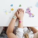 Bras de filles portant des bracelets faits, des perles, des pompons et un porte-clés licorne.