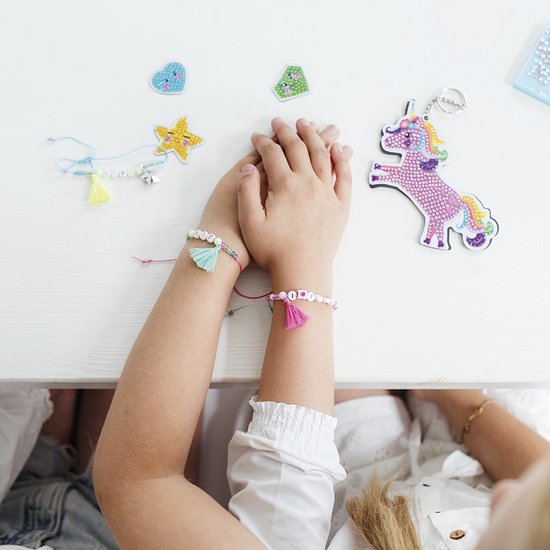 Bras de filles portant des bracelets faits, des perles, des pompons et un porte-clés licorne.