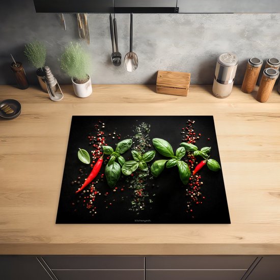 Zwarte inductiebeschermer met basilicum, rode pepers en peperkorrels op een houten aanrecht.