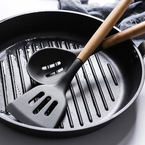 Spatule grise avec fentes et louche grise sur une poêle grill noire.