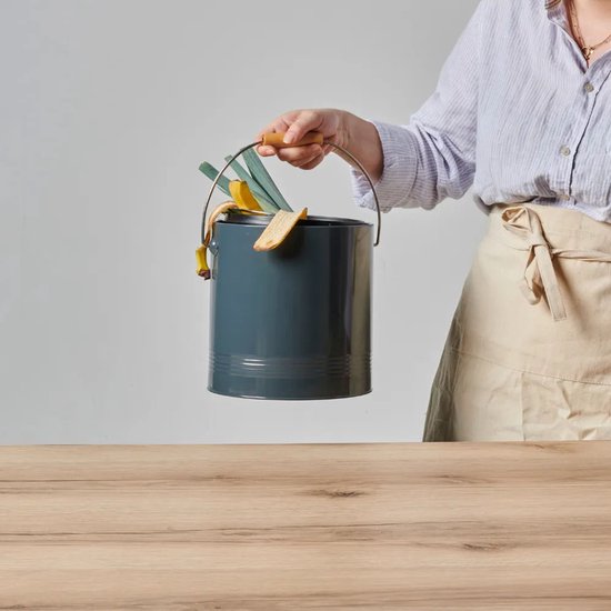 Donkere grijze compostbak met houten handvat, gevuld met bananenschillen, brood en groenten.
